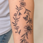 Florales Fineline-Tattoo mit Namen am Unterarm